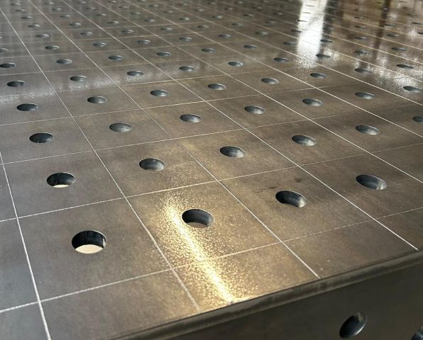 Widok z bliska metalowej powierzchni z siatką i regularnie rozmieszczonymi okrągłymi otworami.