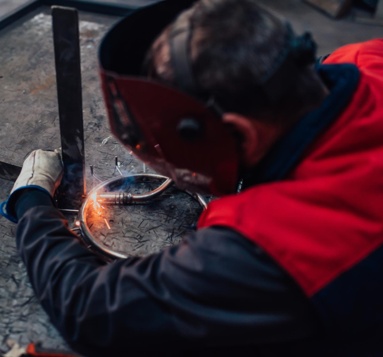 Osoba nosząca odzież ochronną spawa metal na stole warsztatowym, wytwarzając iskry.